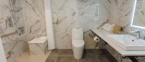 A bathroom with a shower, toilet, sink, and marble walls.