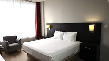 Une chambre d’hôtel avec un grand lit, une chaise, une table de chevet et une lampe.