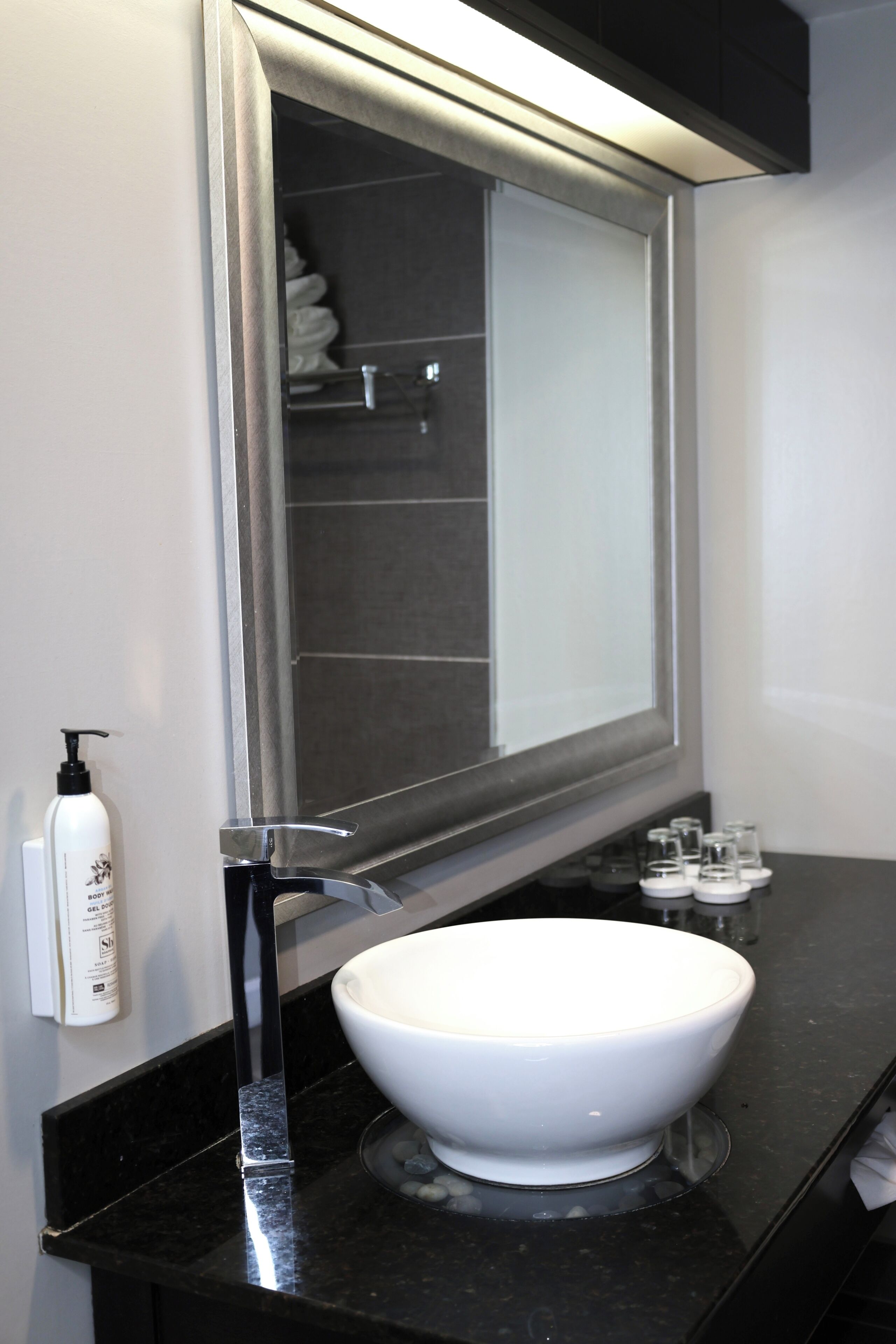 A bathroom with a white sink, a large mirror, and a bottle of soap on the countertop.