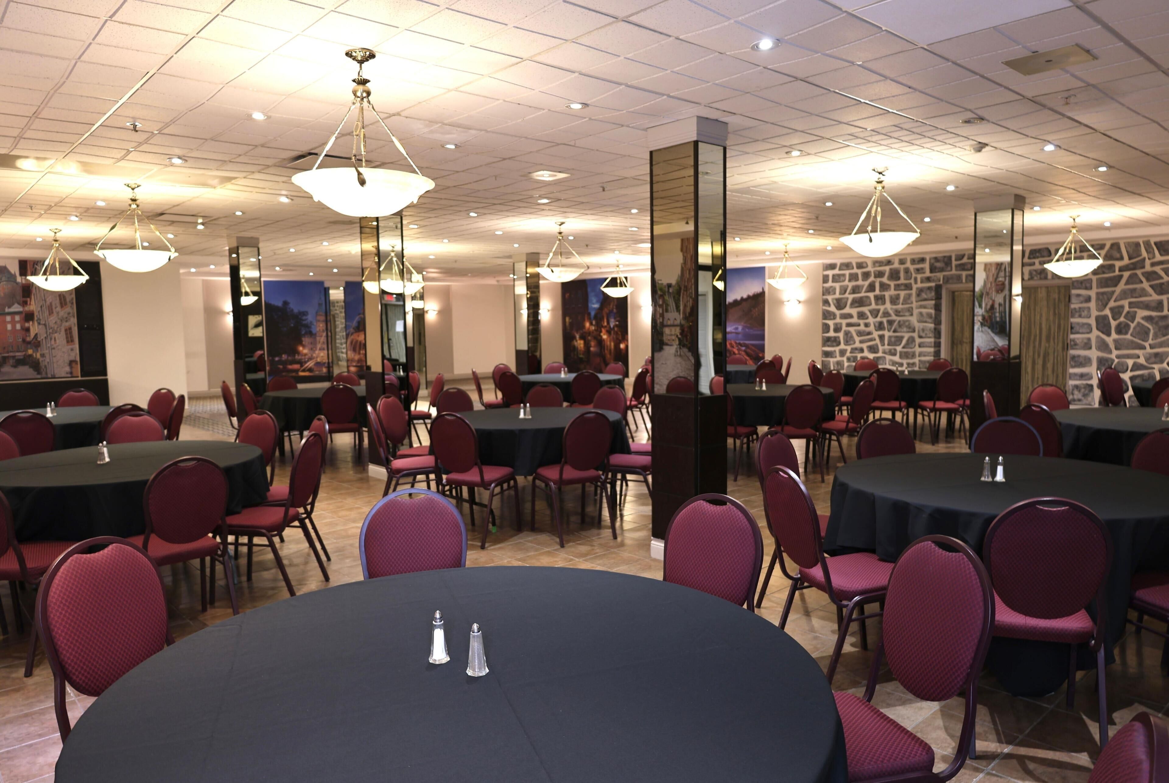 Une salle de conférence avec des tables rondes et des chaises rouges, équipée de lampes de table et dotée d’un mur en pierre.
