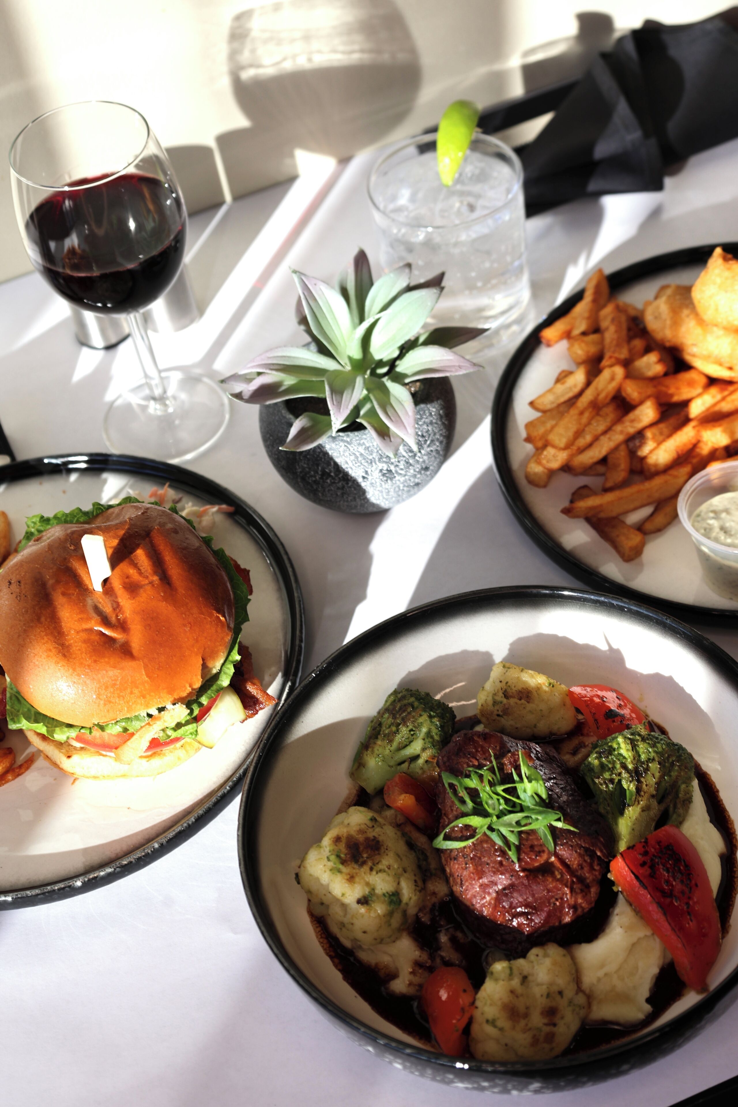 A table with a burger, fries, a salad, and a glass of red wine.