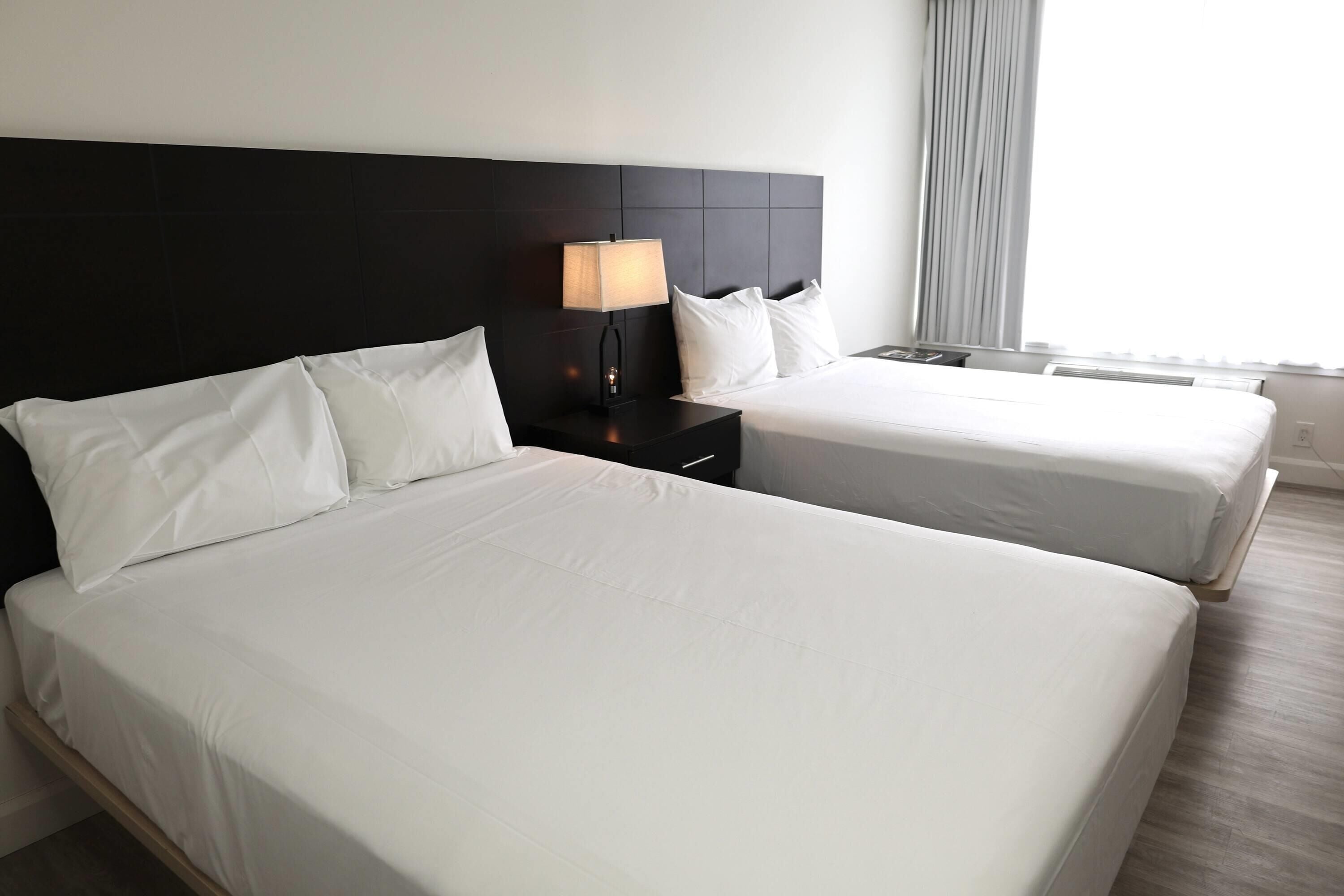 Une chambre d’hôtel avec deux lits, une table de chevet avec une lampe et une fenêtre avec des rideaux.