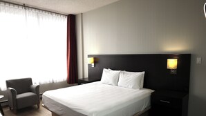 A hotel room with a large bed, a chair, a nightstand, and a lamp. - Travelodge by Wyndham Hotel & Convention Centre Quebec City (Québec City)