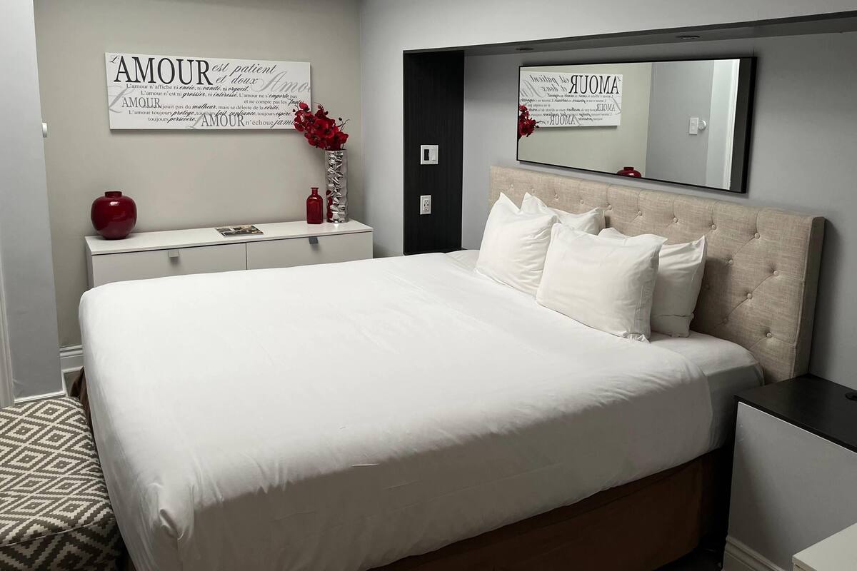 Un dormitorio con una cama grande, una mesita de noche, un aparador, un espejo y una pared con texto.