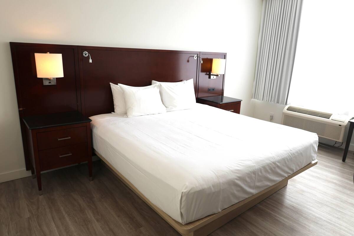Habitación de hotel con una cama grande, dos mesitas de noche con lámparas, un escritorio y una ventana con cortinas.