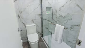 Un baño moderno con cabina de ducha de vidrio, inodoro y perchero para toallas.