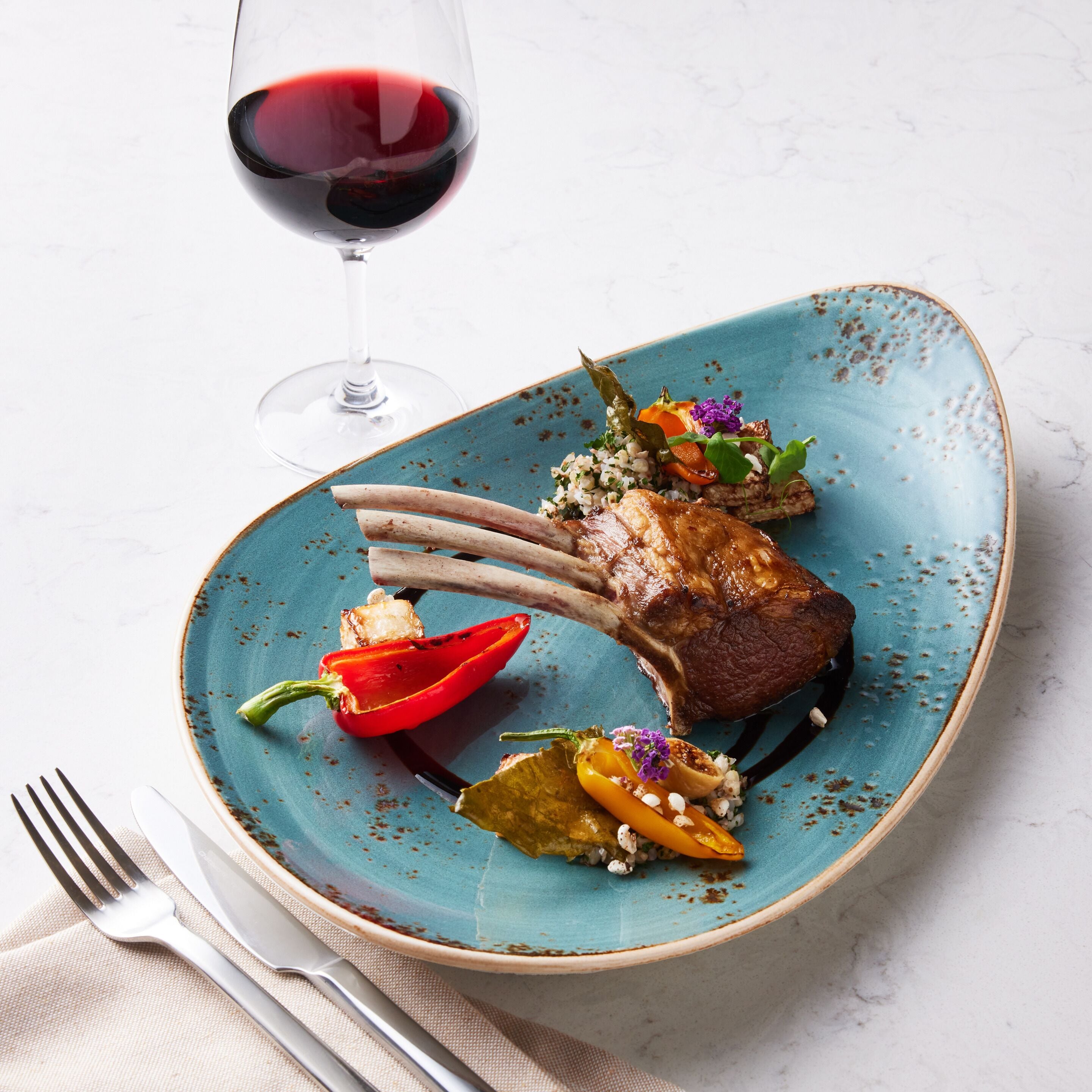 A plate of food with a lamb chop, vegetables, and a glass of red wine.