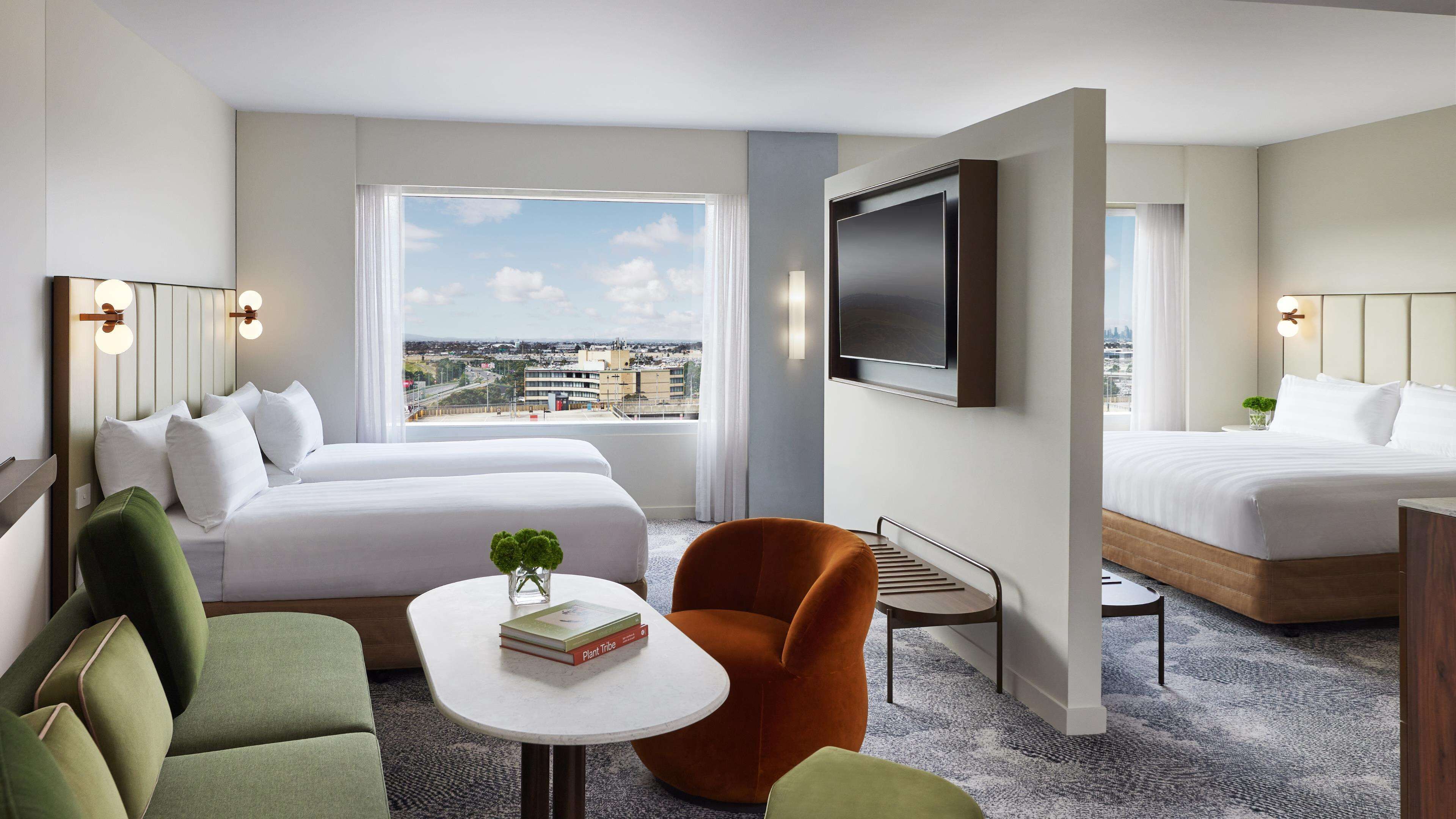 A hotel room with a large bed, a smaller bed, a TV, a desk, and a view of the city.