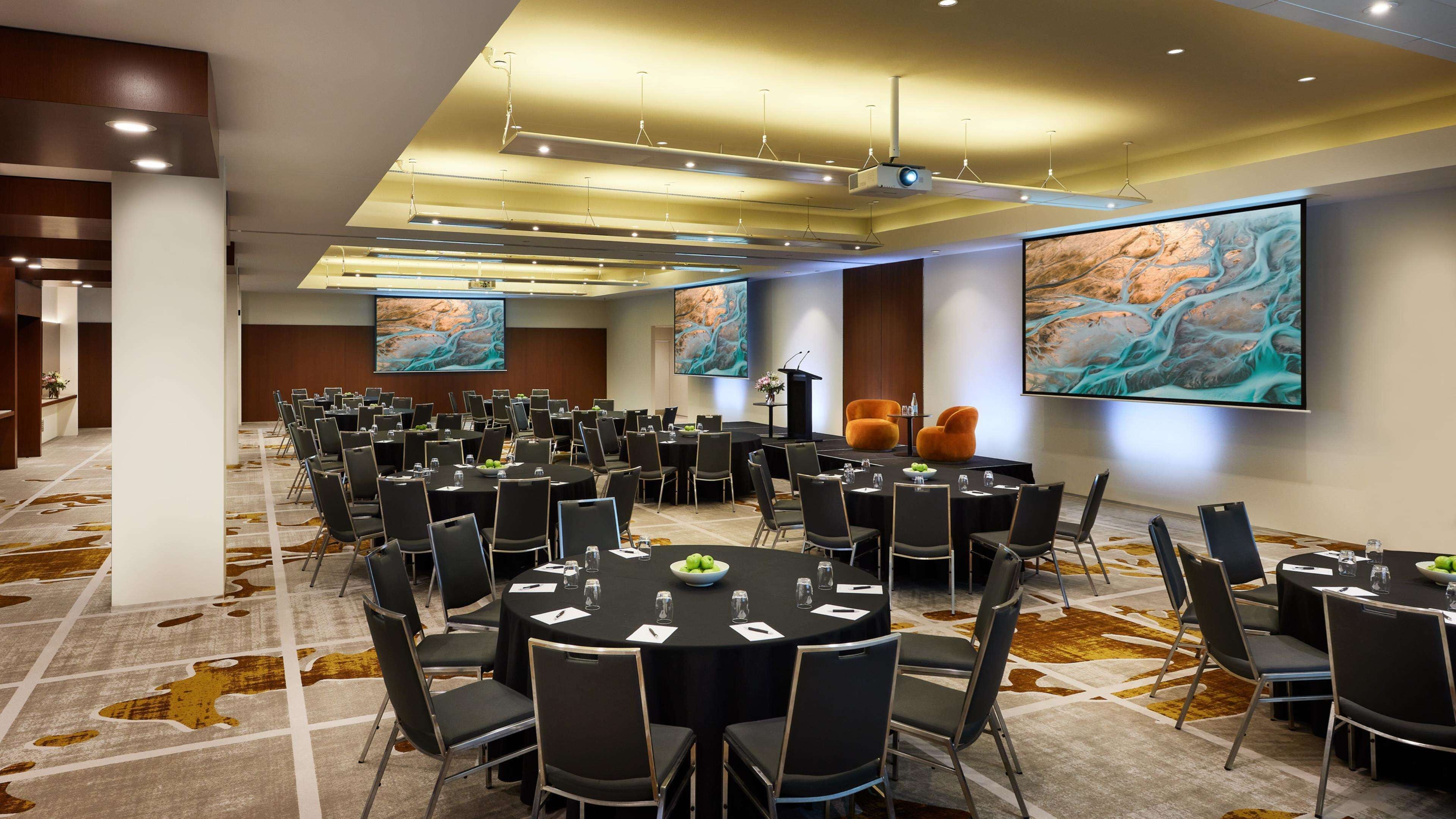 A conference room with multiple tables and chairs, large screens, and a modern ceiling design.