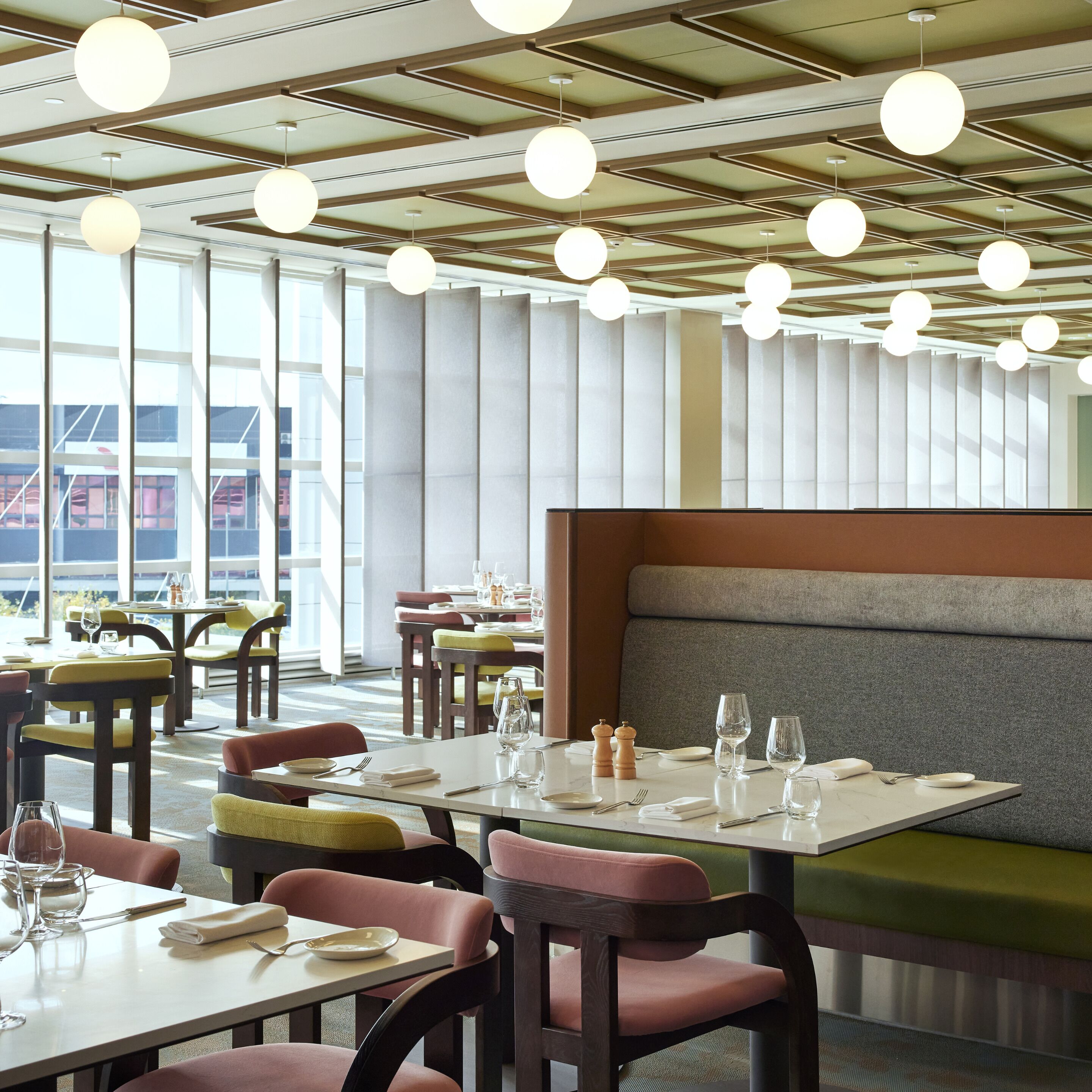 A modern restaurant interior with high ceilings, round pendant lighting, and a mix of seating options including tables and booths.