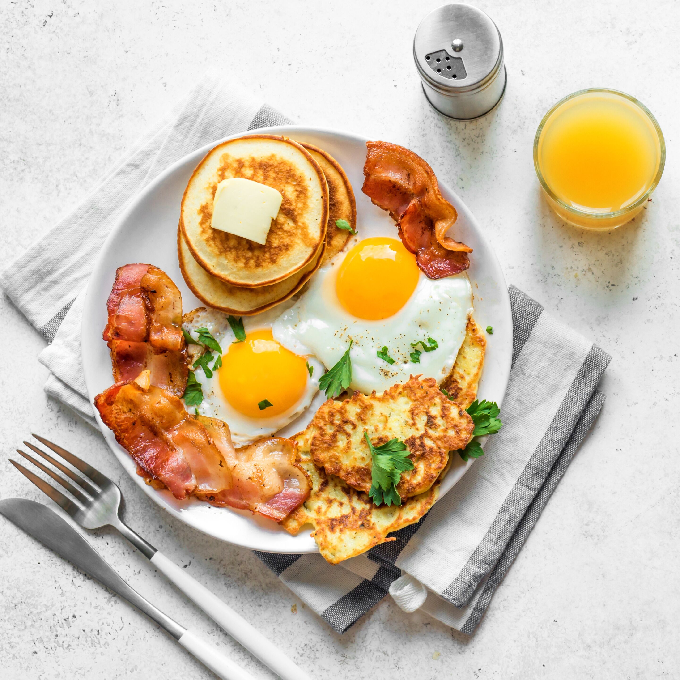 A plate of breakfast with eggs, bacon, toast, and a glass of orange juice.