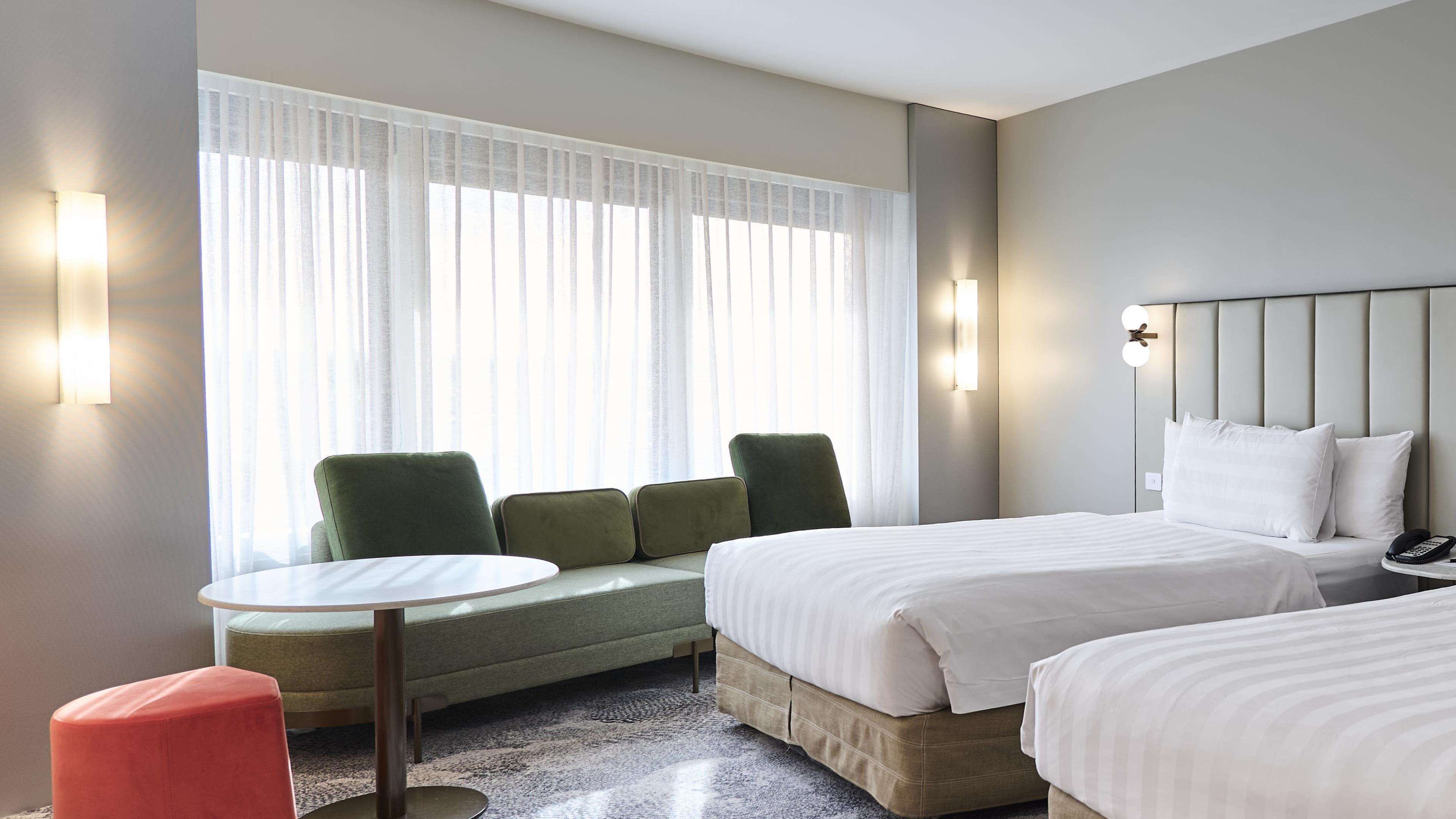 A hotel room with a bed, a small table, two chairs, a sofa, and a window with sheer curtains.