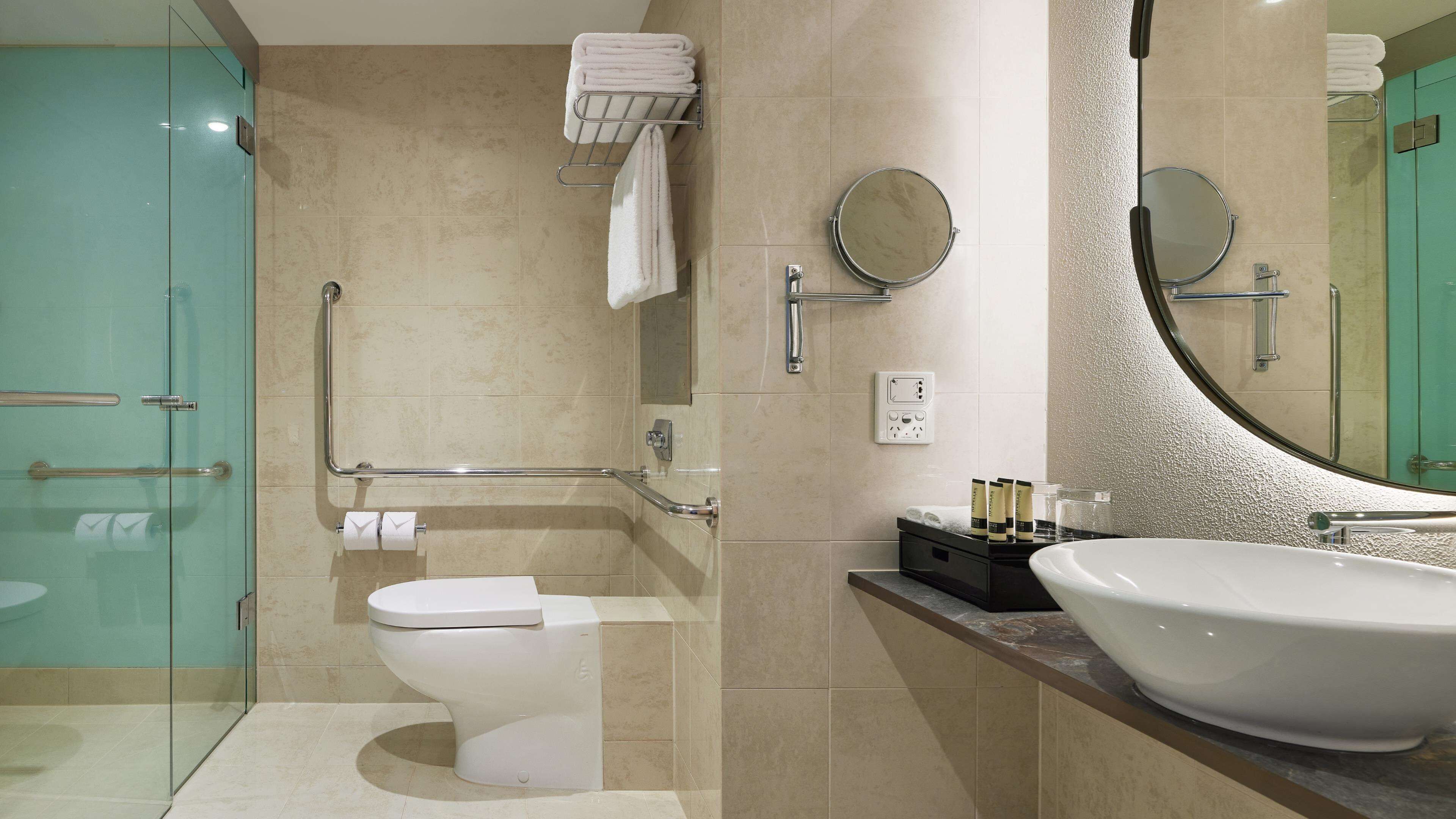 A modern bathroom with a glass shower enclosure, a white toilet, a large sink, and a mirror with a circular frame.