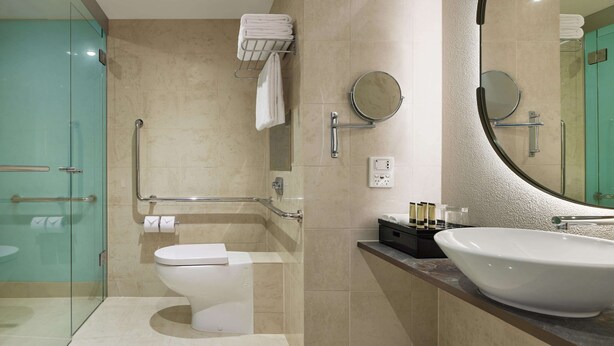 Un baño moderno con cabina de ducha de vidrio, inodoro blanco, lavamanos grande y espejo con marco circular.