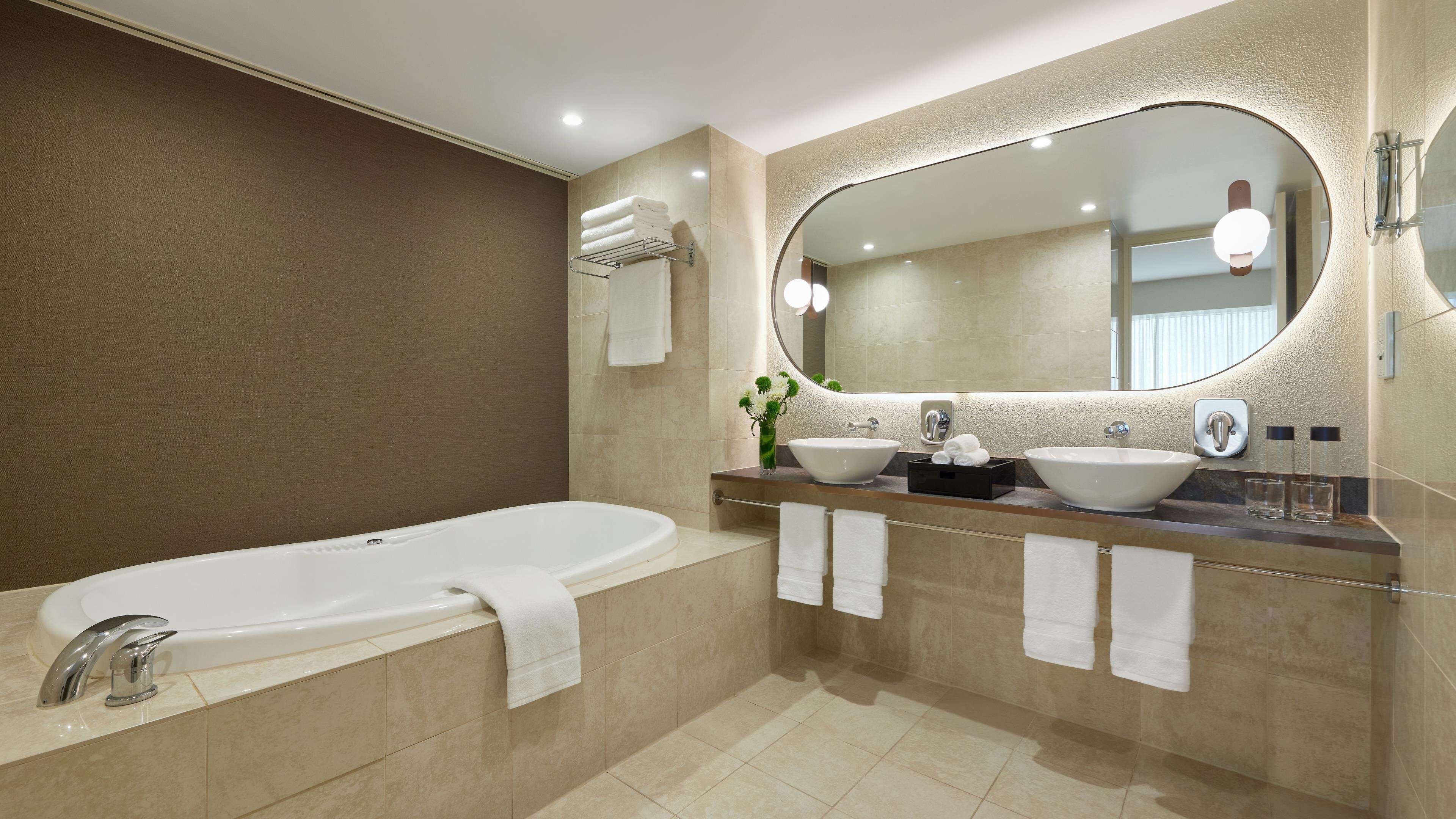 A modern bathroom with a bathtub, two sinks, and a large mirror.
