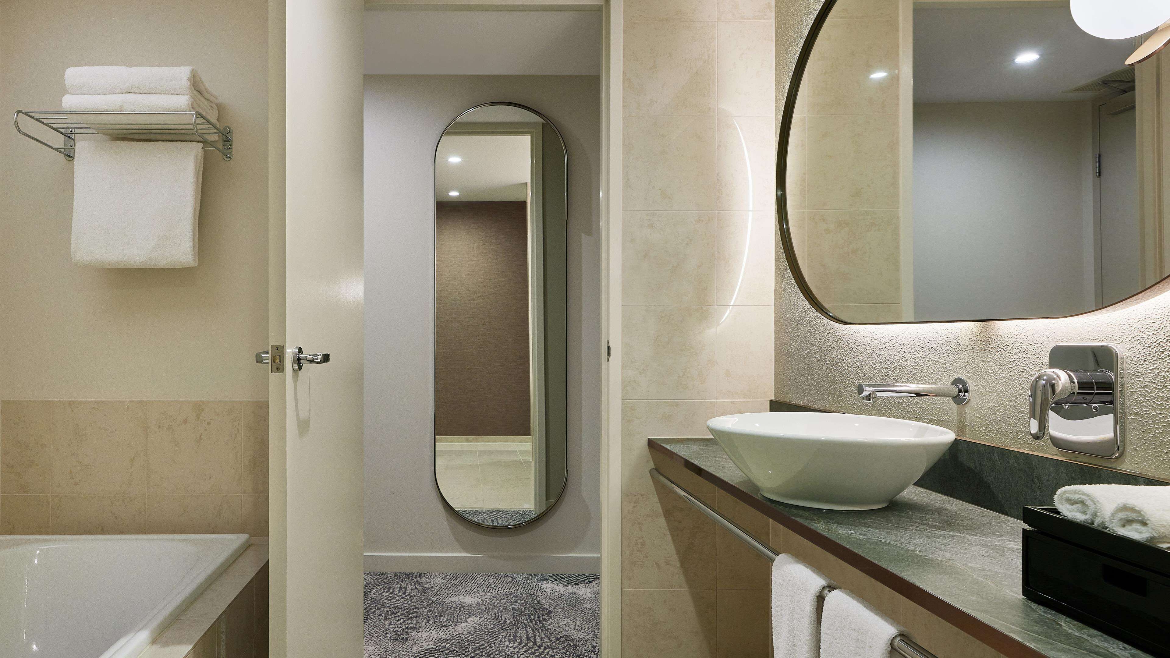 A modern bathroom with a bathtub, a large mirror, and a sink with a towel rack.