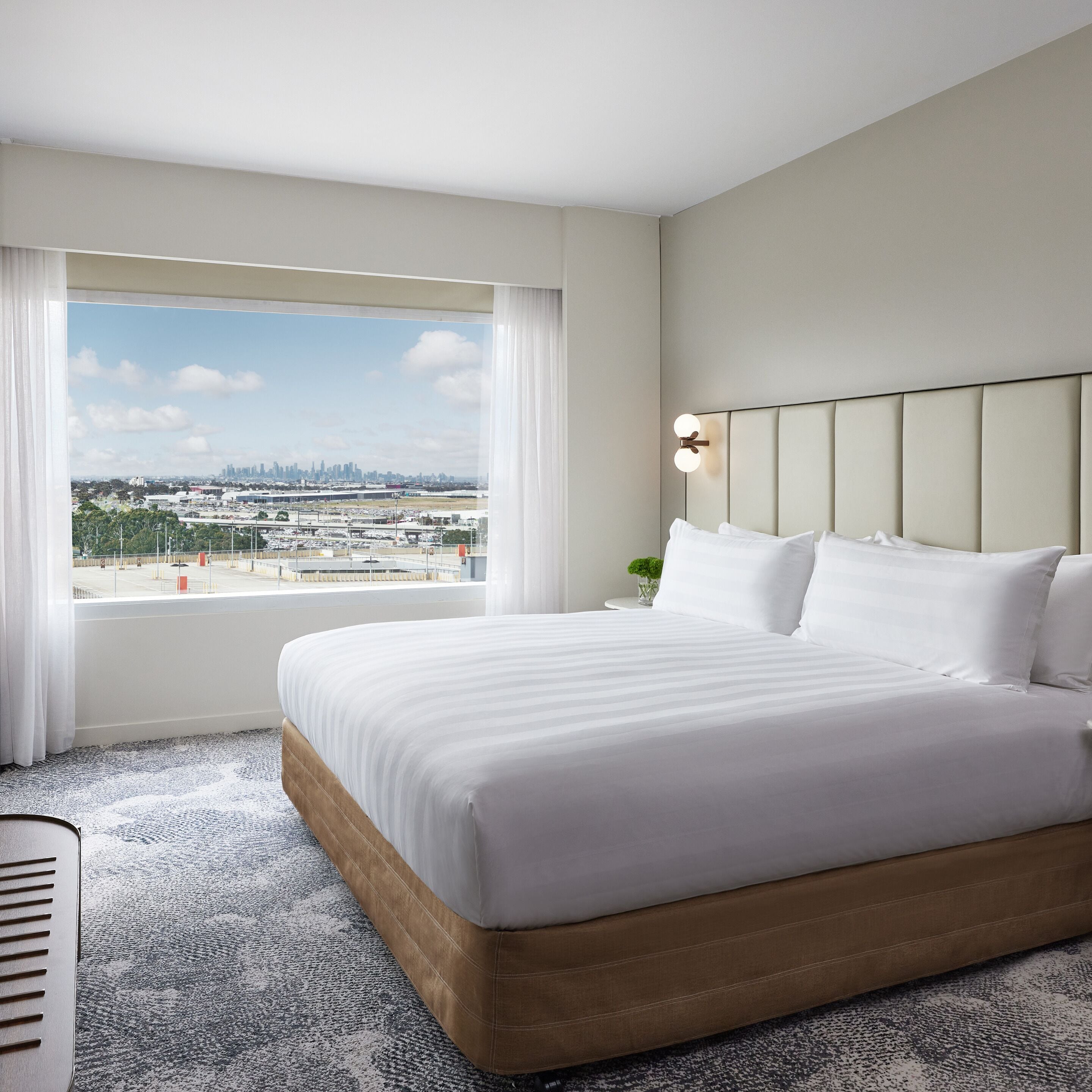 Une chambre d’hôtel avec un grand lit, une vue sur la ville et une table de chevet avec une lampe.