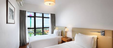 A hotel room with two beds, a large window with a city view, a ceiling light, and a framed picture on the wall.
