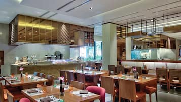 Un restaurant moderne avec des tables et des chaises en bois, un comptoir avec un espace dédié aux boissons et une cuisine ouverte, visible à travers une paroi en verre.