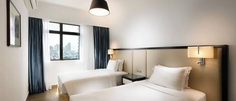 Habitación de hotel con dos camas, vistas a la ciudad, un ventanal grande con cortinas y una lámpara de techo moderna.