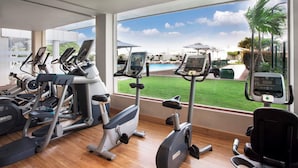 A gym with various exercise machines, large windows, and a view of a pool and lawn. - Hilton Colombo Residence (Colombo)