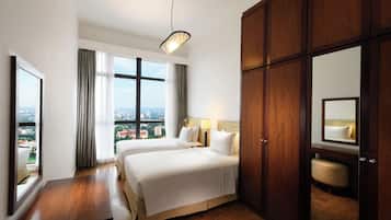 A hotel room with two beds, a wooden wardrobe, a bedside table, a mirror, and a view of the city.