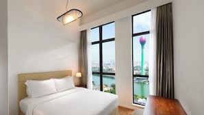 A hotel room with a large bed, a desk, and a view of a cityscape and tower through the window.