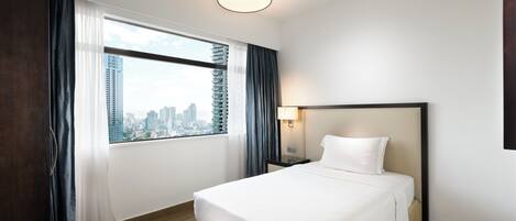 A hotel room with a large bed, a nightstand, a lamp, a window with curtains, and a city view.