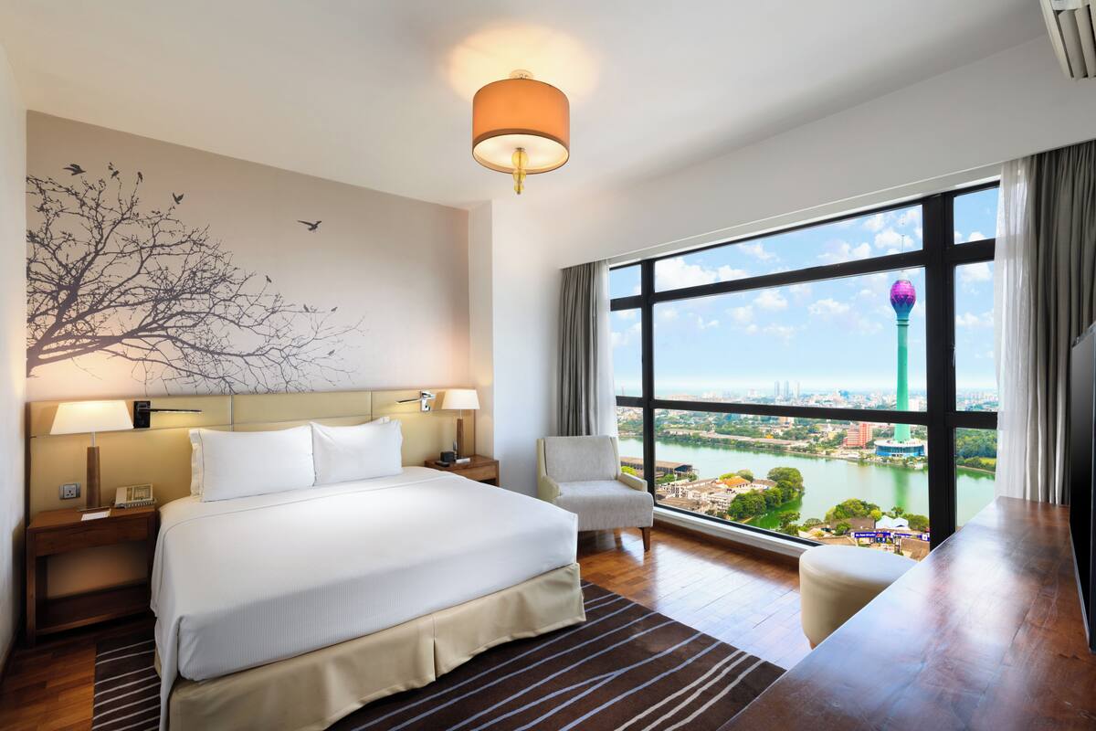 A hotel room with a large bed, two bedside tables with lamps, a chair, a view of a cityscape and a river.