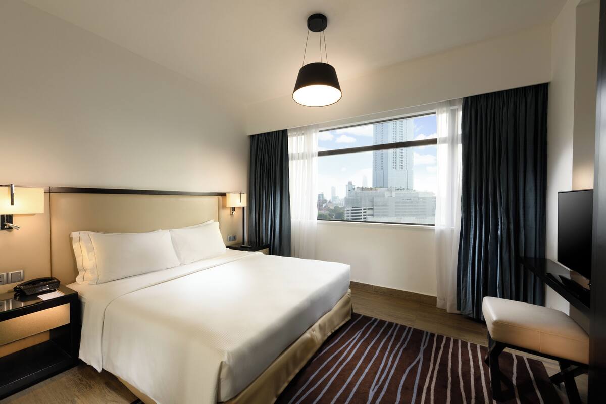 A hotel room with a large bed, a TV, a desk with a phone, and a window with curtains.