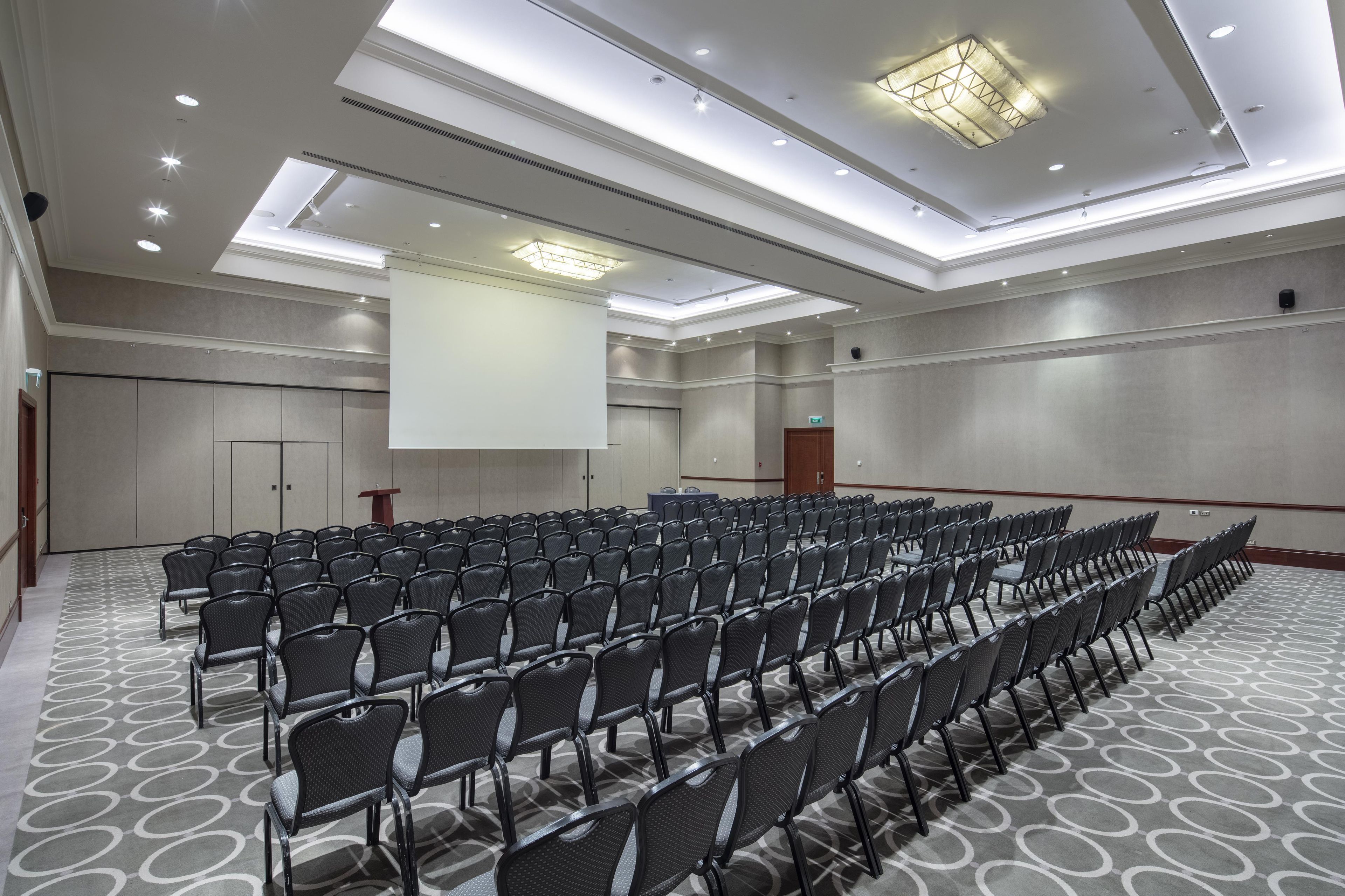 Ein Konferenzraum mit Reihen von Stühlen, einem Rednerpult und einer großen Leinwand.