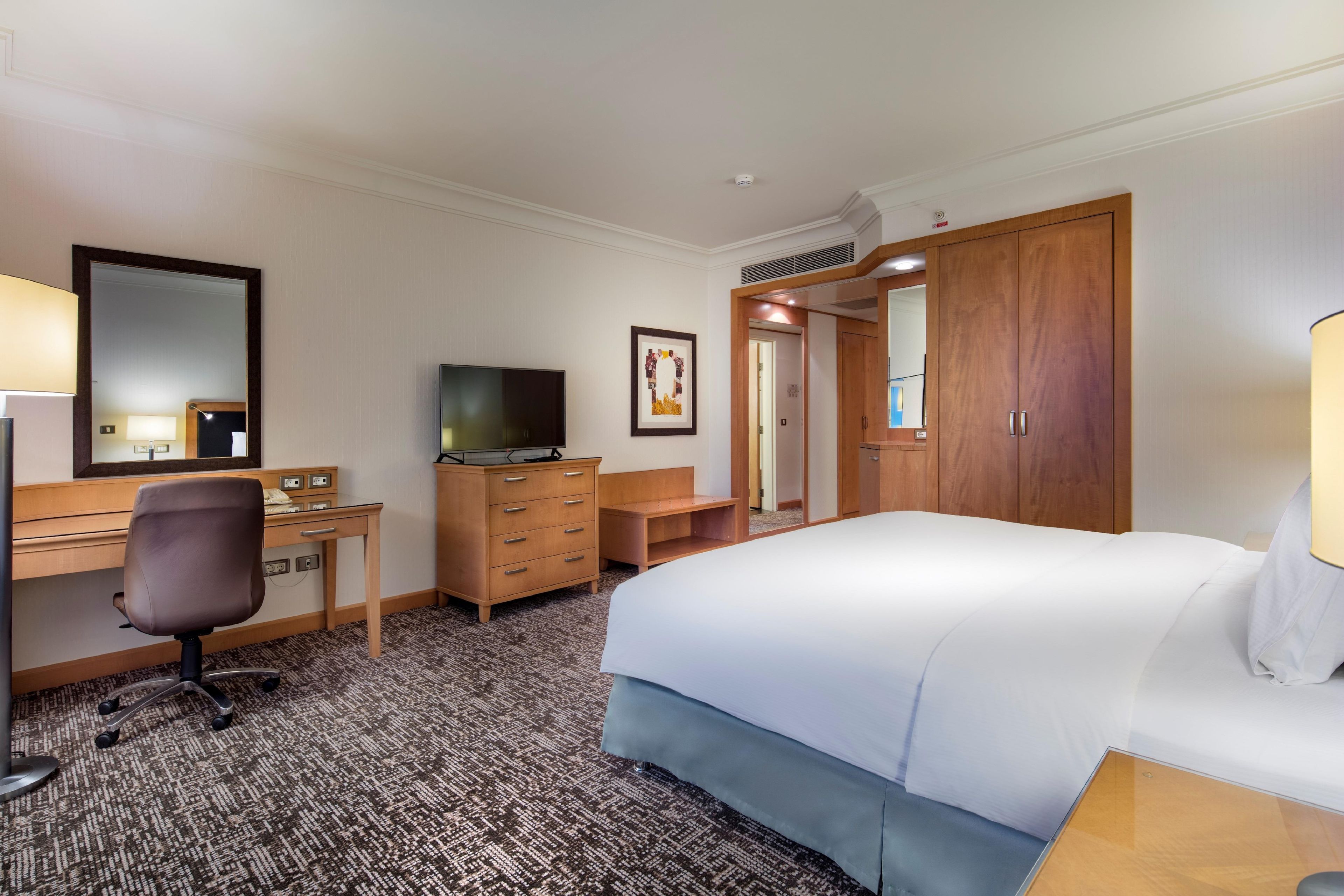 A hotel room with a bed, desk, chair, television, dresser, and a door leading to another room.