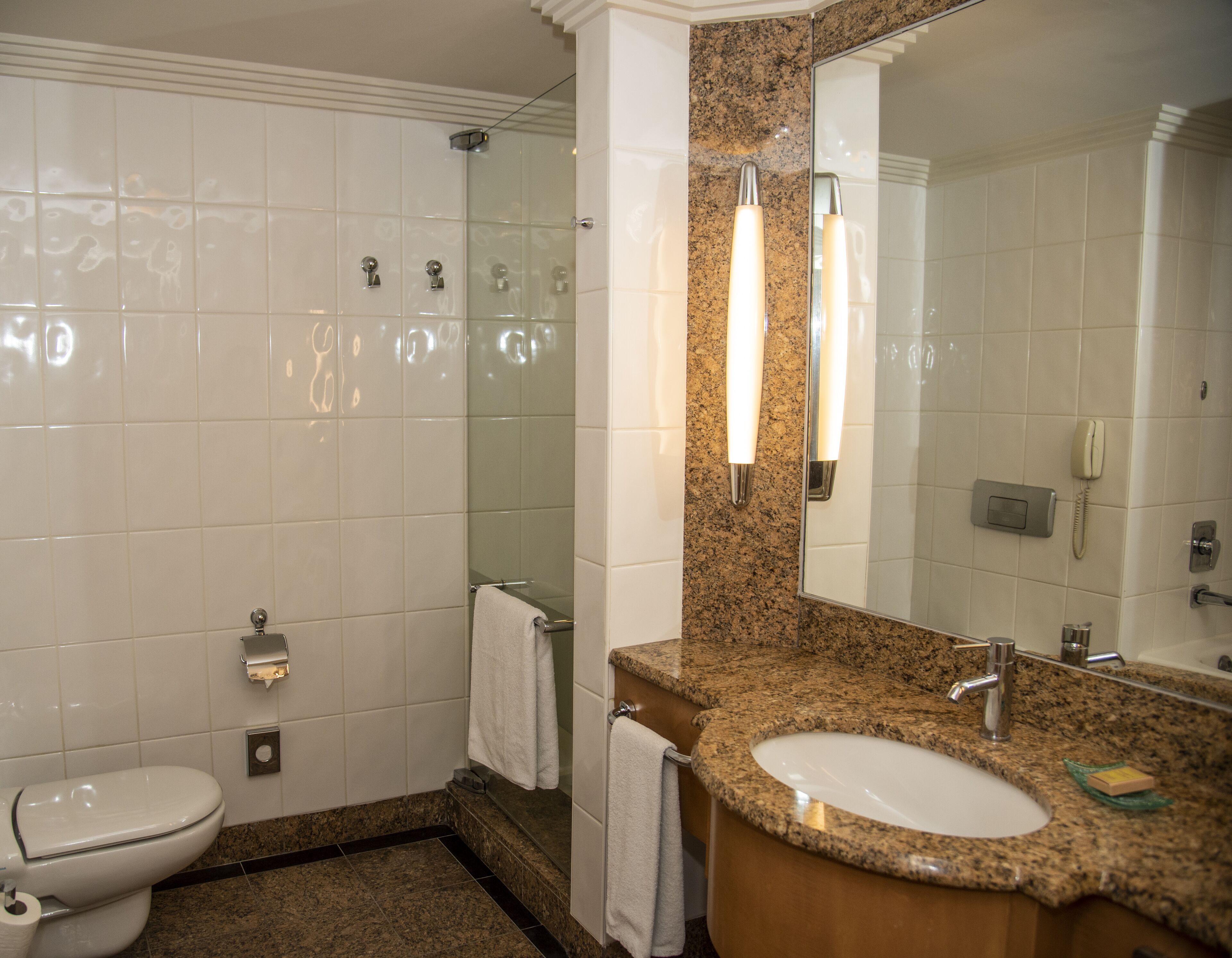 A bathroom with a toilet, sink, mirror, and shower.