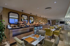 Eine moderne Hotelhalle mit Frühstücksbar, Sitzgelegenheiten und einem großen Spiegel, der den Raum widerspiegelt.