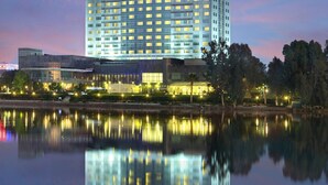 Un hotel moderno de gran altura, con el logotipo de Hilton bien visible, múltiples pisos y un reflejo en el agua.
