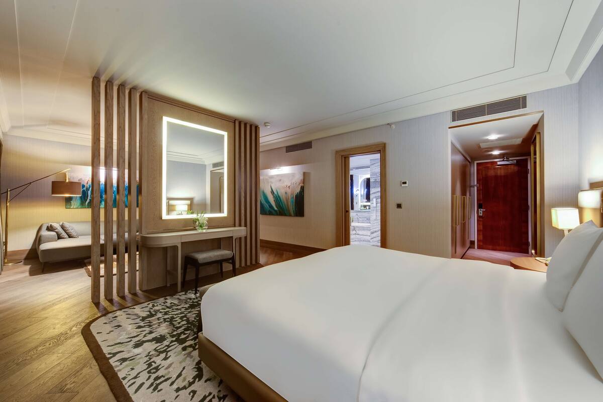 A hotel room with a large bed, a desk with a chair, a sofa, a mirror, and a painting on the wall.