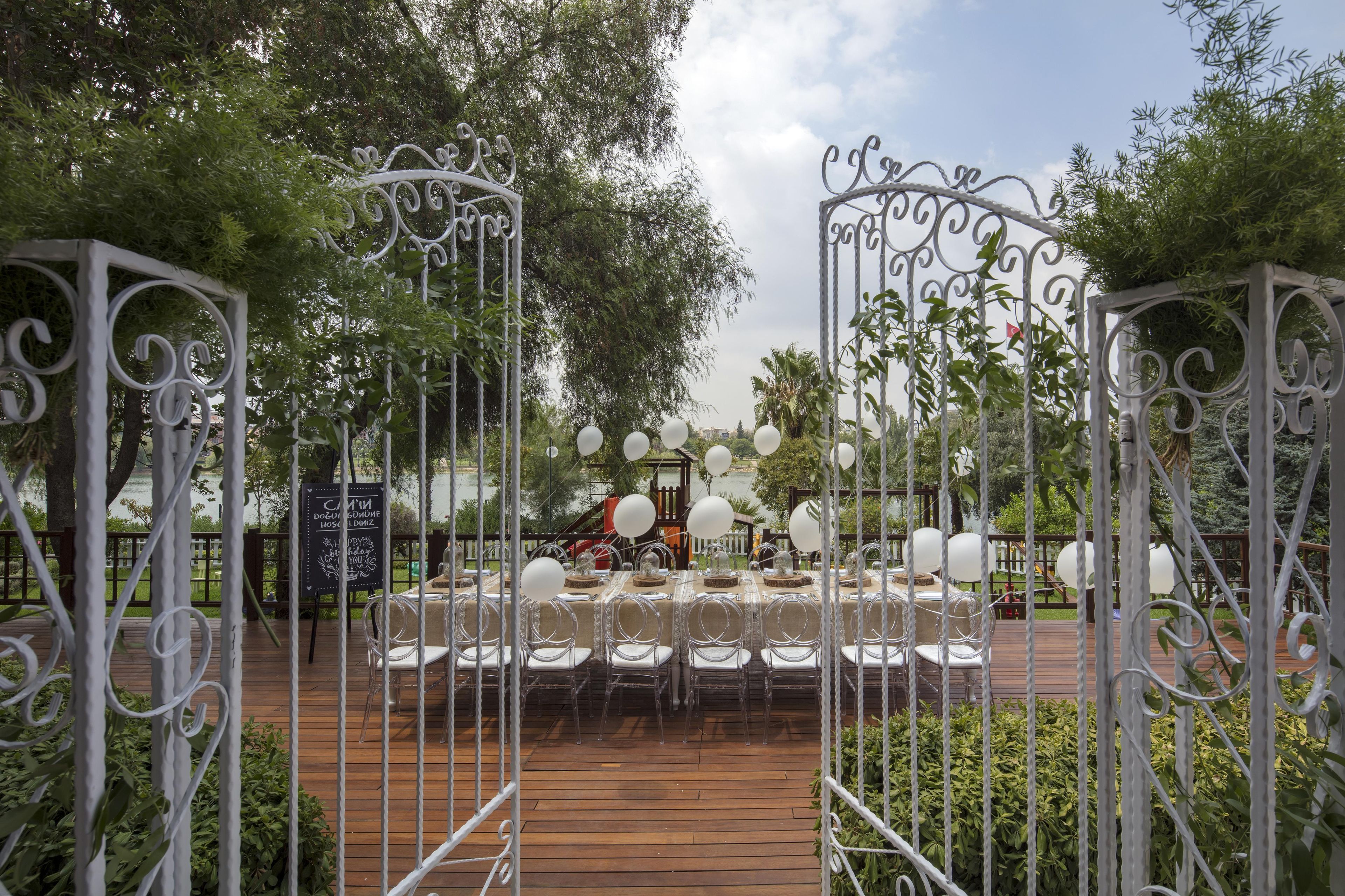Un área de comedor al aire libre con una terraza de madera, portones de metal y mesas dispuestas para una comida.