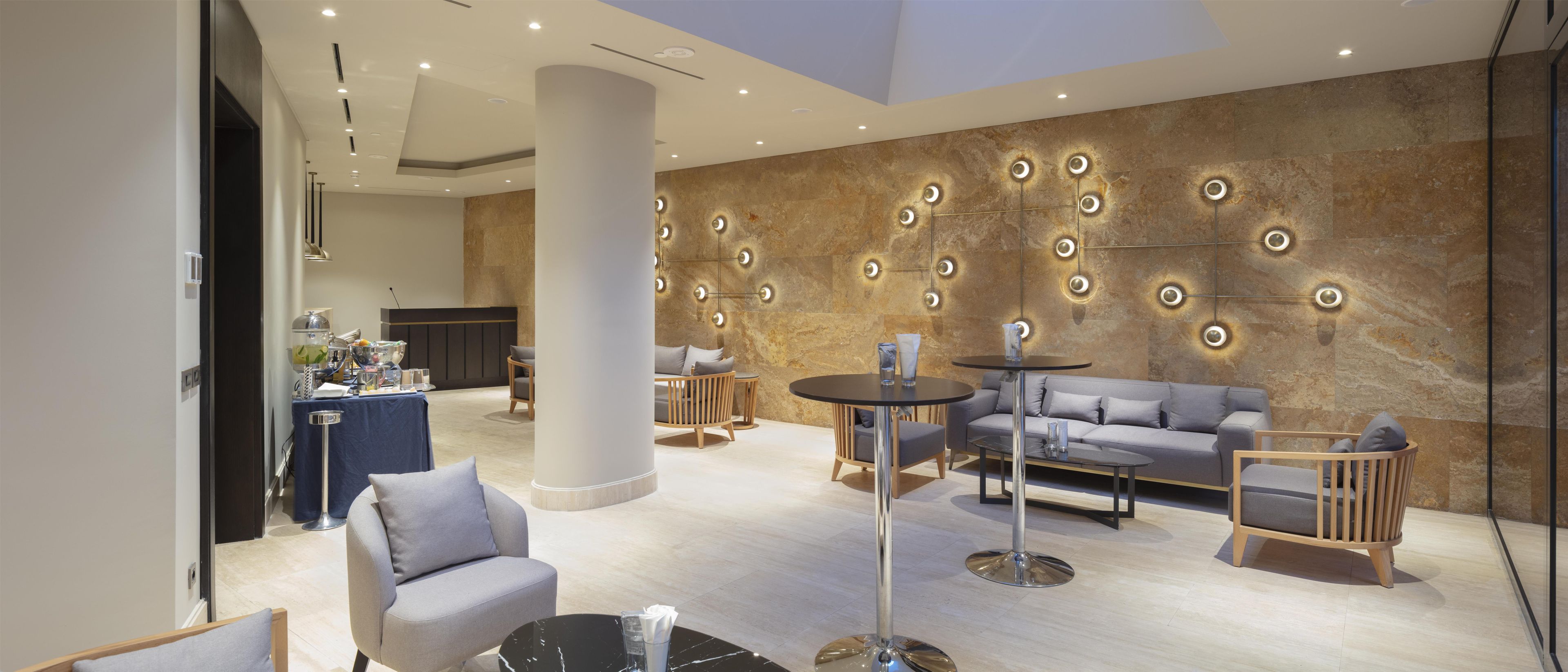 A modern lounge area with seating, a buffet, and a decorative wall with circular light fixtures.