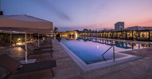 Ein Poolbereich mit Liegestühlen und Sonnenschirmen, einem kühlen Pool und umgebenden Gebäuden.