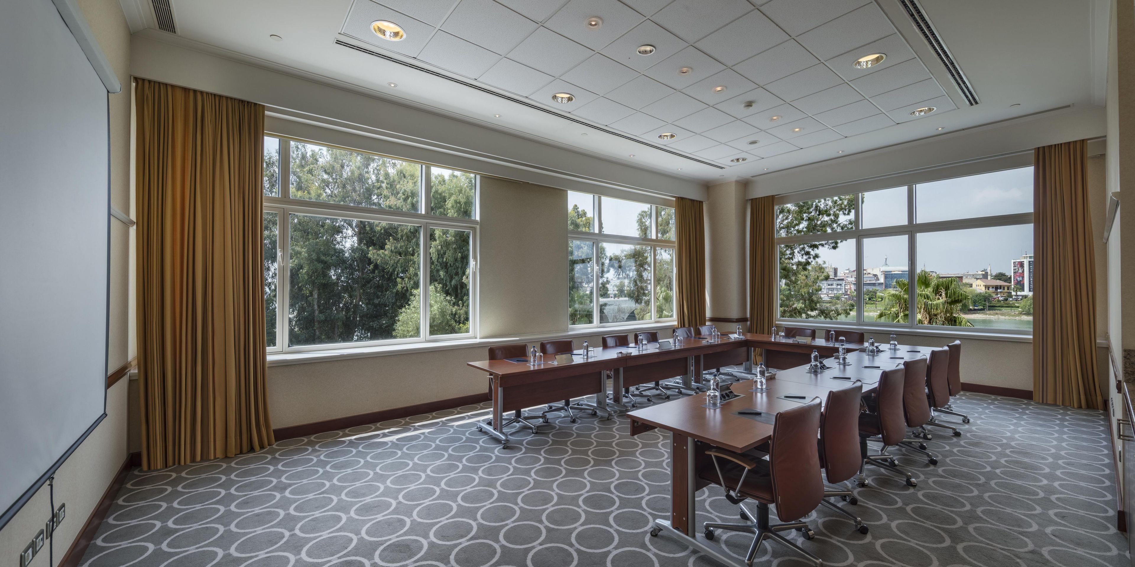 A conference room with a large table, chairs, and a view of the outdoors through large windows.
