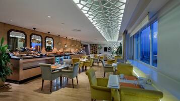 A modern hotel lobby with a breakfast bar, seating area, and large windows.