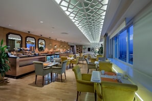 Un moderno vestíbulo de hotel con barra de desayuno, zona de estar y ventanas amplias.