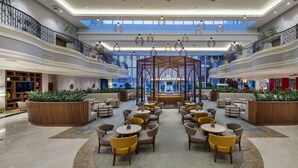 Un espacio interior amplio con varias disposiciones de asientos, una estructura decorativa central y vistas al exterior a través de grandes ventanales.