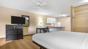Una habitación de hotel con cama, escritorio, televisión, armario y kitchenette.