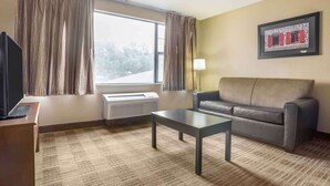 A hotel room with a sofa, a coffee table, a TV, a window with curtains, a radiator, and a framed picture on the wall.