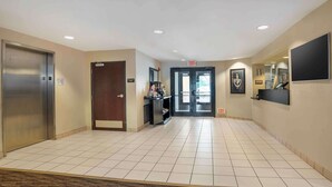 A hotel lobby with a tiled floor, an elevator, a reception desk, and an exit door.
