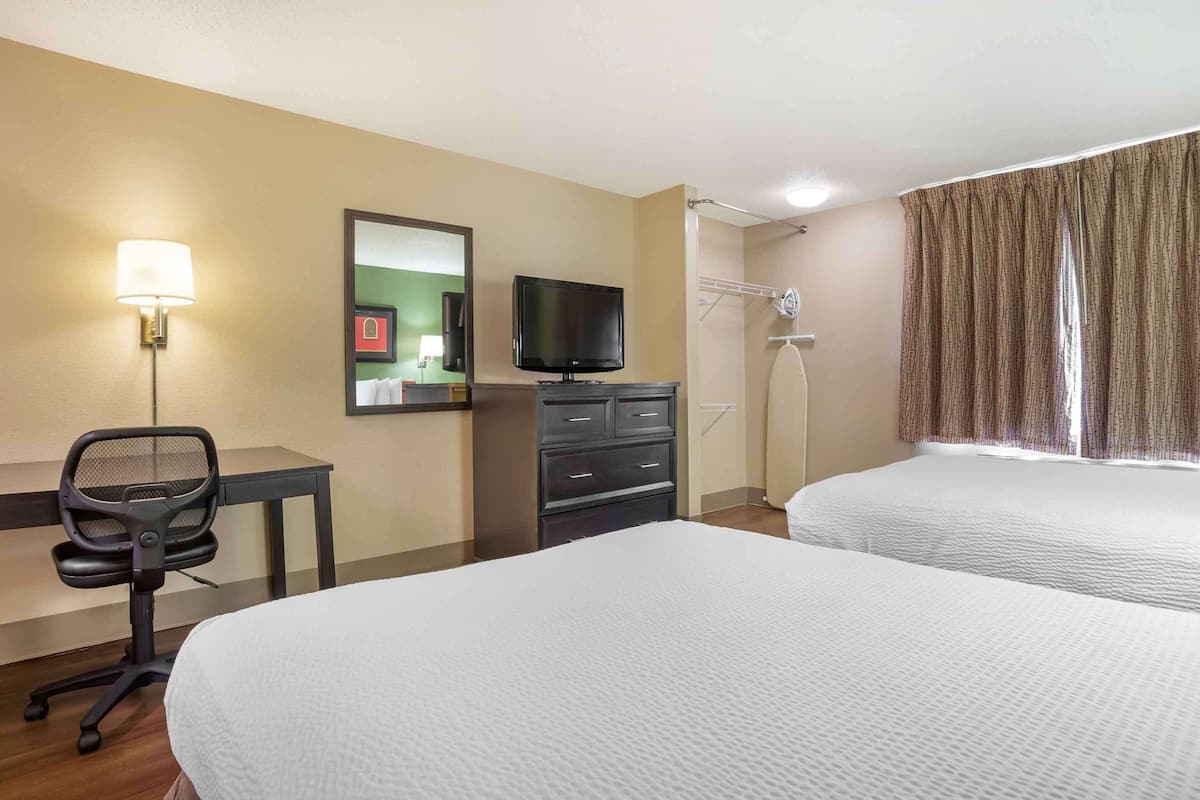 A hotel room with two beds, a desk with a chair, a television, and a mirror.