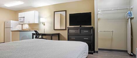 A hotel room with a bed, a desk, a television, a microwave, and a shower area.