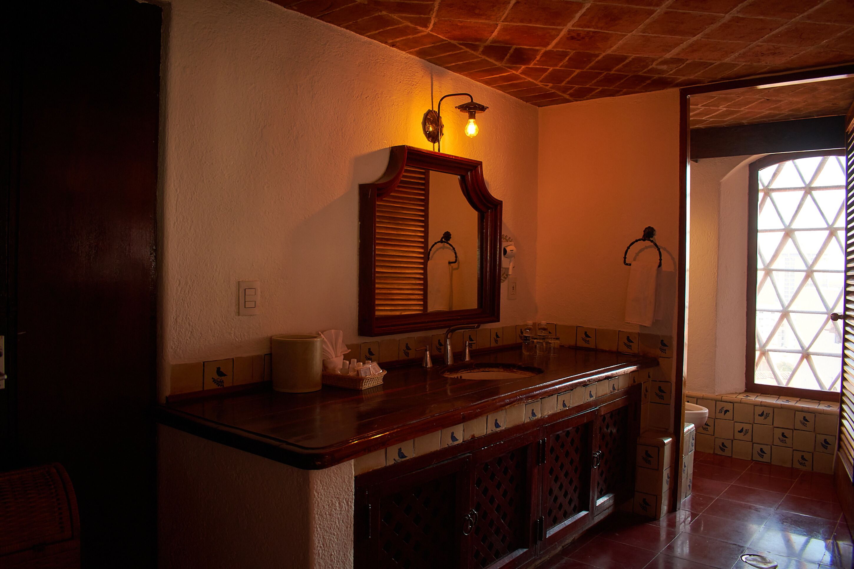 A bathroom with a wooden vanity, a large mirror, and a window with a geometric pattern.