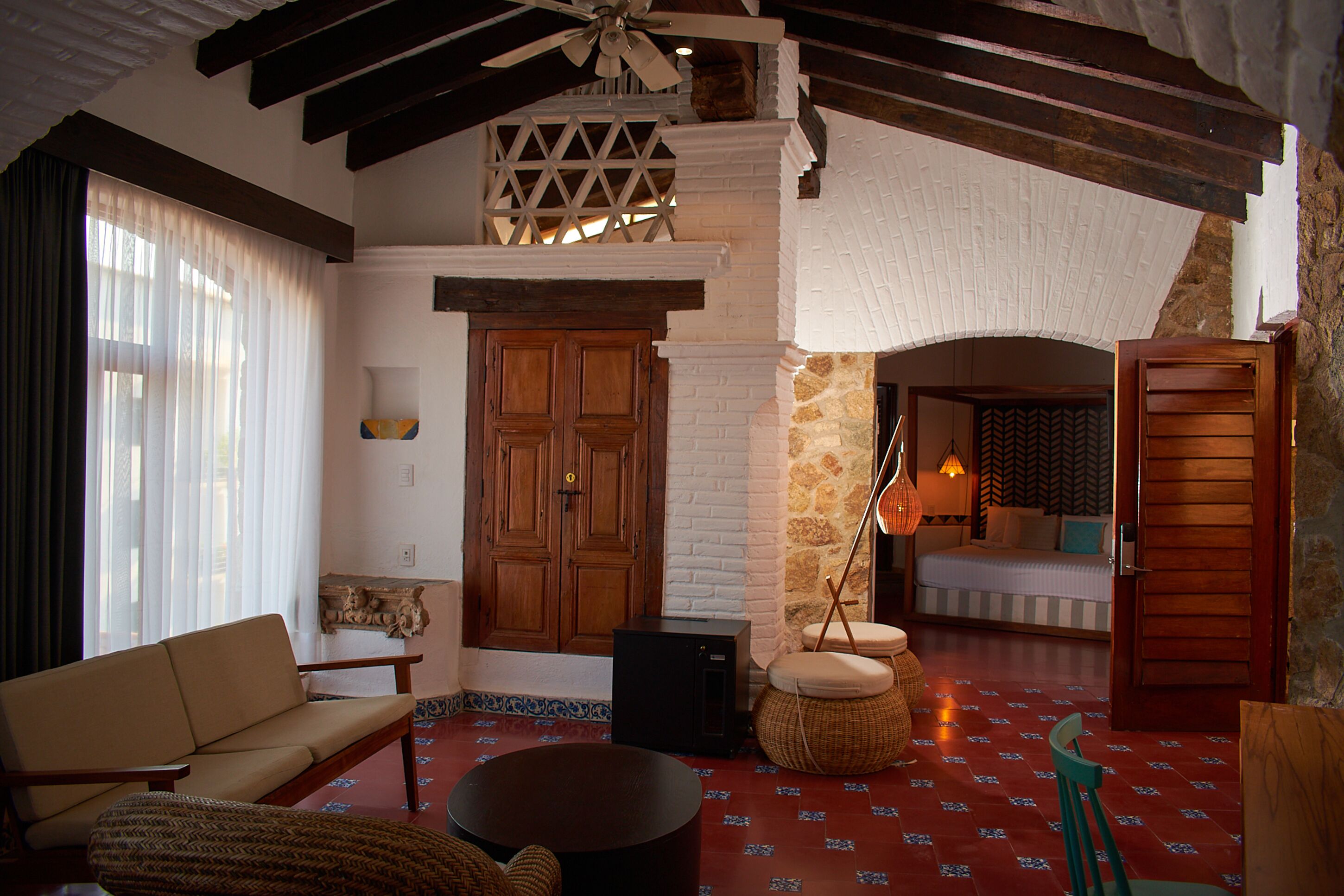 A cozy room with a sofa, ottoman, and a small table. There is a wooden door and a window with curtains.